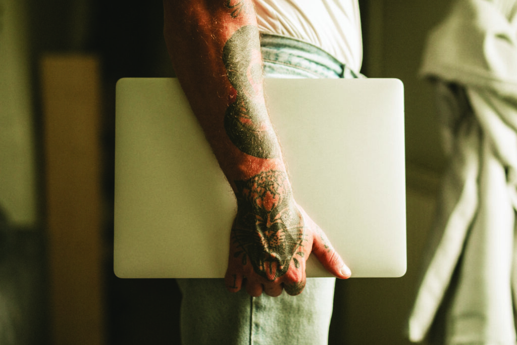Image of a man's arm with tattoos holding a laptop.